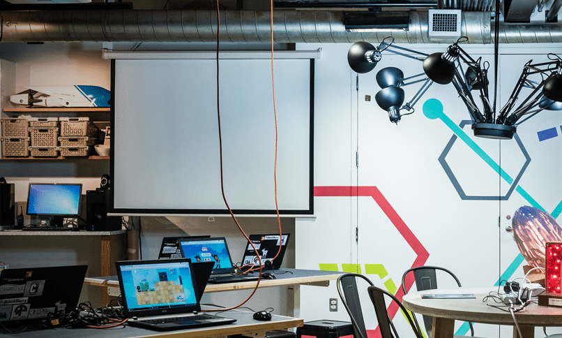Computers a projector screen and tables in the Underground Studio MakerSpace